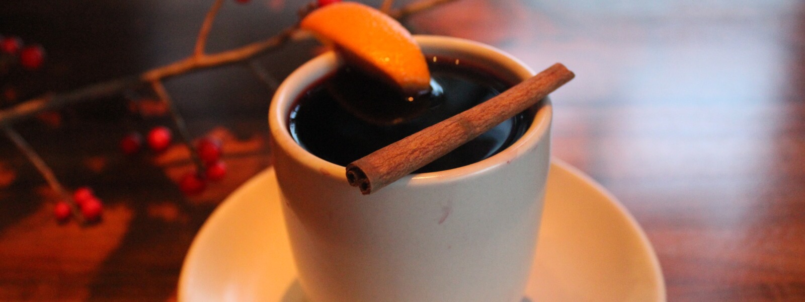 Cup of mulled wine with citrus wedge and cinnamon stick.