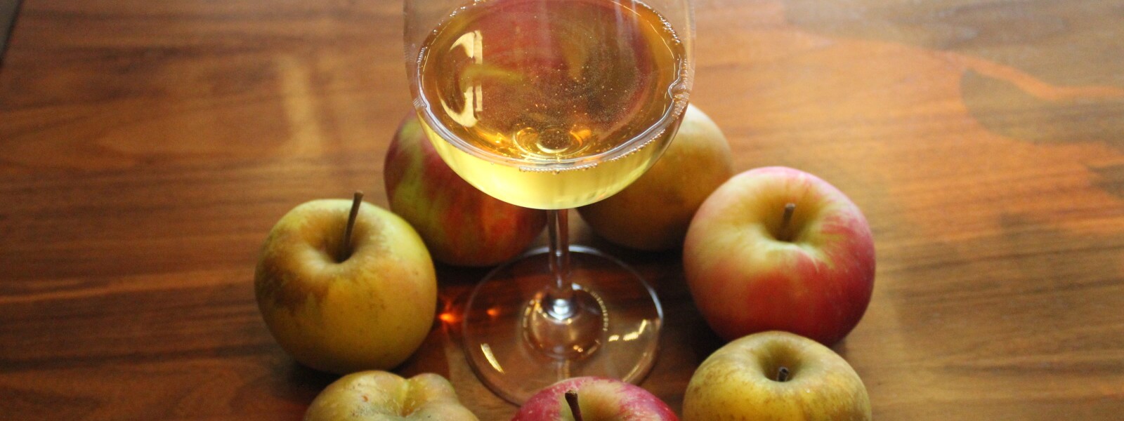 7 apples surrounding a glass of cider.
