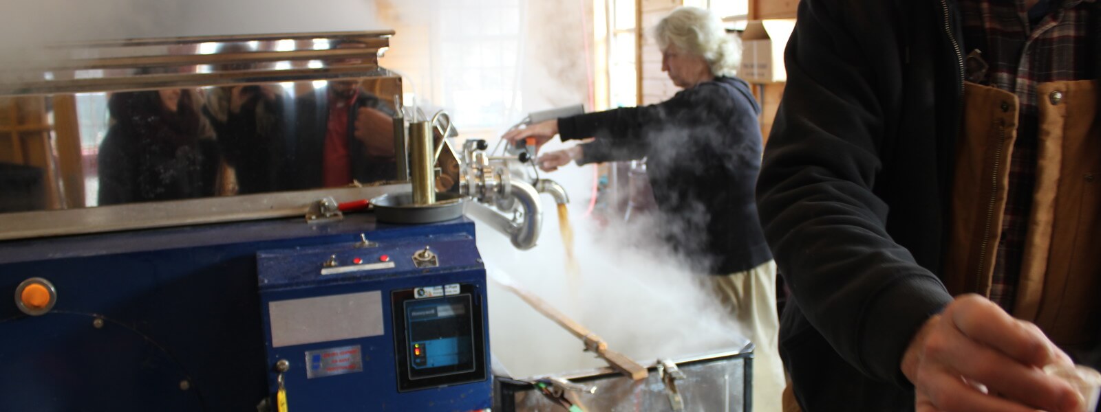 Person stirring maple syrup in vat in the sugar shack.