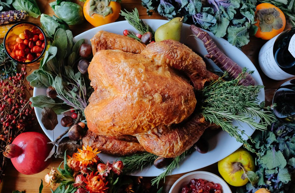 Overhead shot of turkey filled with herbs and surrounded by fresh produce.