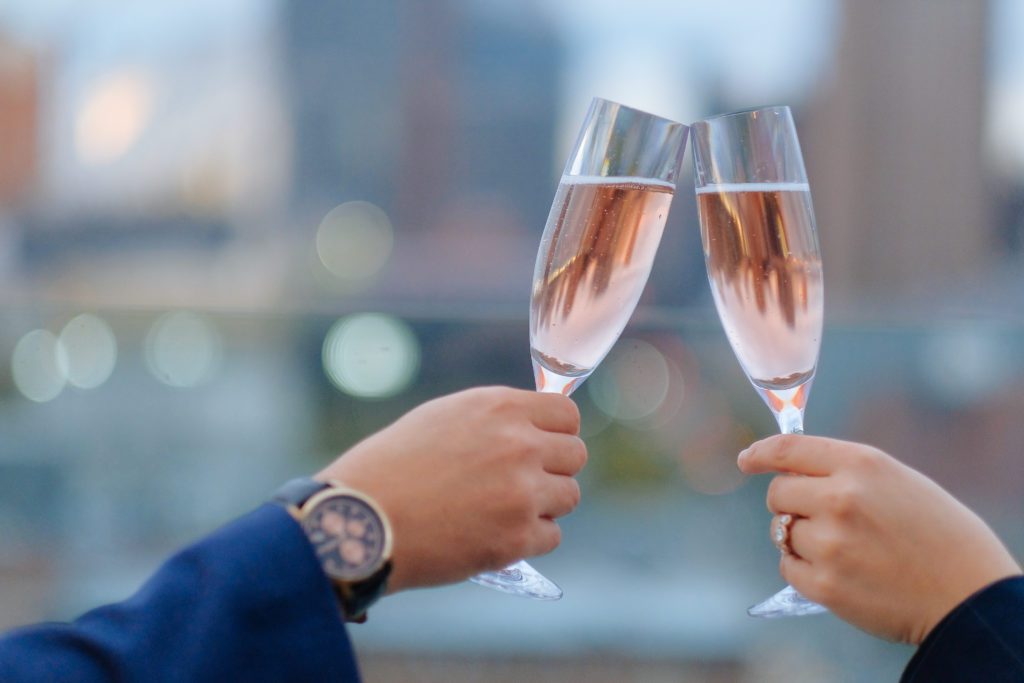 Two hands toasting with rosé in champagne flutes.